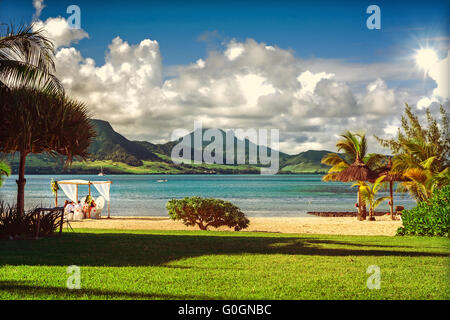 Piccolo gruppo di nozze presso una spiaggia tropicale con vegetazione lussureggiante Foto Stock