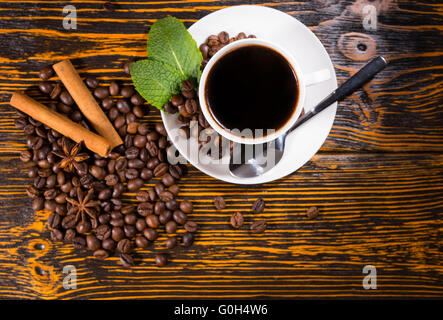 Angolo alto ancora la vita di bianco tazza e piattino contenenti caffe' macinato di fresco in appoggio sulla tavola in legno rustico Top sparse con chicchi di caffè tostati, bastoncini di cannella e anice stellato. Foto Stock