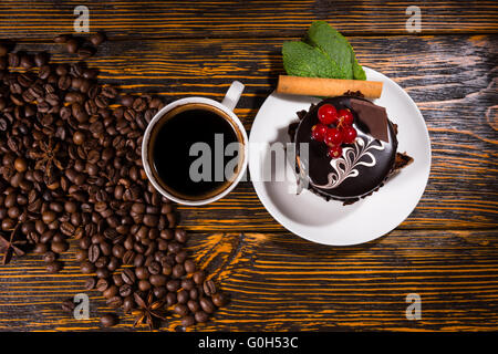 Vista aerea di gustosi dessert al cioccolato sulla piastra bianca dalla tazza da caffè e fagioli distribuiti su tavola di legno Foto Stock