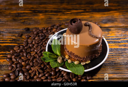 Delizioso piccolo cilindro torta al cioccolato a forma di fetta nel piatto circondato da chicchi di caffè su tinto scuro dello sfondo in legno Foto Stock