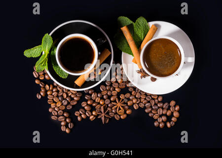 Vista dall'alto in basso di set di preparazione per tè e caffè circondato da fagioli con condimenti su piattini su sfondo nero Foto Stock