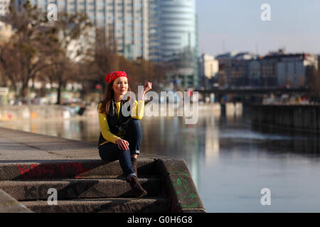 Bella donna asiatica in maglione giallo e rosso con velo seduti su un fiume in una città europea Foto Stock