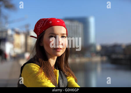 Bella donna asiatica in maglione giallo e rosso con velo seduti su un fiume in una città europea Foto Stock