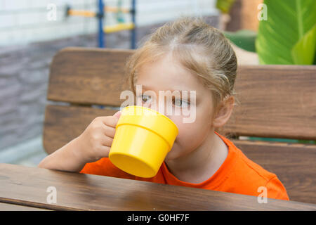 Quattro-anno-girl bevendo un drink seduti a tavola in veranda Foto Stock