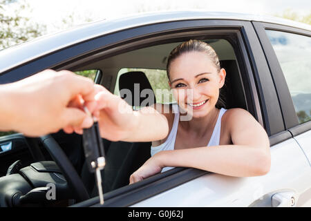 Giovane donna sorridente seduto in macchina prendendo la chiave Foto Stock