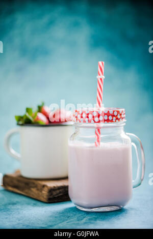 Frullato di fragole in vaso vintage con red spogliato di paglia blu su sfondo vivace Foto Stock