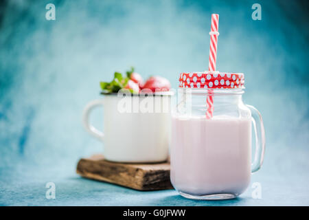 Frullato di fragole in vaso vintage con red spogliato di paglia blu su sfondo vivace Foto Stock