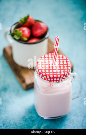 Frullato di fragole in vaso vintage con red spogliato di paglia blu su sfondo vivace Foto Stock