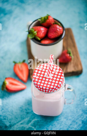 Frullato di fragole in vaso vintage con red spogliato di paglia blu su sfondo vivace Foto Stock