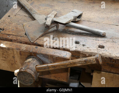 Gli antichi strumenti piccoli ax e grande martello sul vecchio banco in legno con una morsa Foto Stock