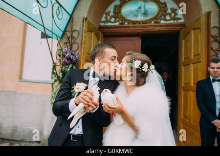 Happy sposi sposa e lo sposo con le colombe in mani sulle porte della chiesa sullo sfondo Foto Stock