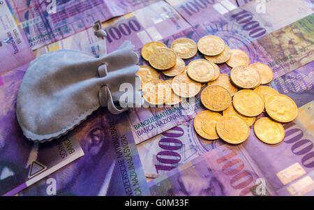 Molti 20 franchi monete d oro colato fuori di una piccola borsa su 1000 franchi svizzeri di banconote. Foto Stock