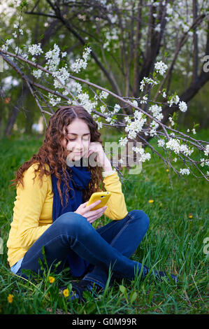 Bella giovane donna seduta su erba con uno smartphone Foto Stock