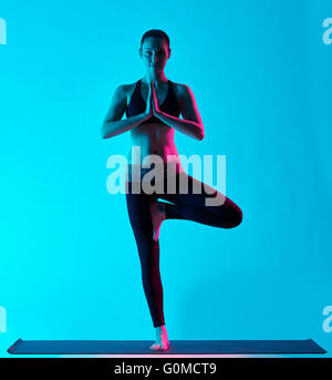 Una donna caucasica esercitando la posizione dell'albero Vriksasana esercizi di yoga in silhouette studio isolato su sfondo blu Foto Stock