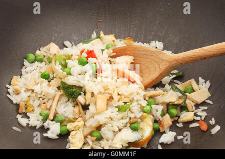 Primo piano del pollo, uova e vegetali di riso fritto in un wok con un cucchiaio di legno Foto Stock