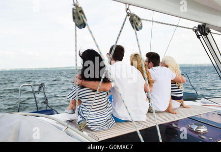 Happy amici vela e seduto sul ponte dello yacht Foto Stock