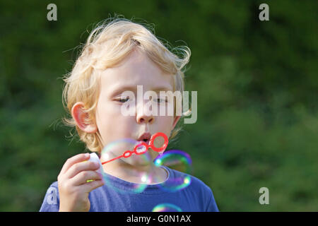 Ragazzo biondo facendo bolle di sapone al di fuori (sfondo verde) Foto Stock