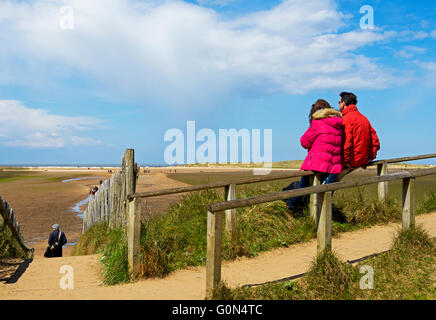 Coppia giovane seduto sulla recinzione che si affaccia sulla spiaggia di Holkham, Norfolk, Inghilterra, Regno Unito Foto Stock