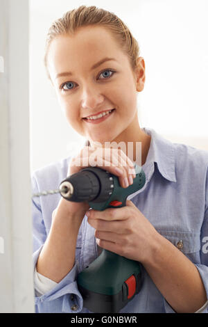 Giovane donna utilizzando un trapano elettrico in Casa di ristrutturazione progetto Foto Stock