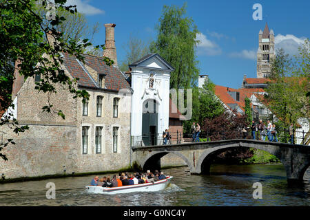 Ingresso al Begijnhof (torre di San Salvatorskerk in background), canal e imbarcazione turistica Bruges, Belgio Foto Stock