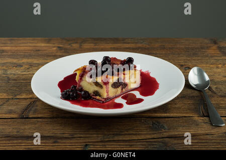 Il budino con le prugne secche, le uve secche di Corinto sulla parte superiore di una piastra bianca su una tavola di legno Foto Stock