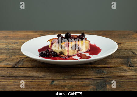 Il budino con le prugne secche, le uve secche di Corinto sulla parte superiore di una piastra bianca su una tavola di legno Foto Stock