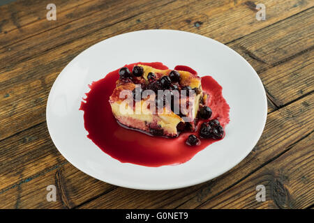 Il budino con le prugne secche, le uve secche di Corinto sulla parte superiore di una piastra bianca su una tavola di legno Foto Stock