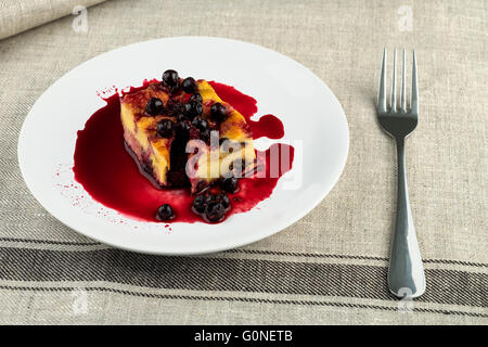 Il budino con le prugne secche, le uve secche di Corinto sulla parte superiore di una piastra bianca su un lino grigio igienico Foto Stock