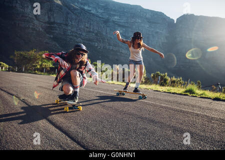 Felice giovani amici divertendosi con lo skateboard. Giovane uomo e donna pattinaggio insieme in una giornata di sole. Foto Stock