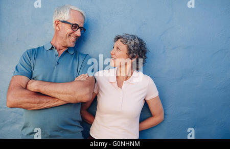 Ritratto di affettuosa coppia matura guardando ogni altra contro sfondo blu. Amare medio di età compresa tra uomo e donna in piedi Foto Stock