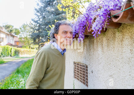 Uomo di mezza età in azzurro camicia e maglione verde vicino impianto di glicine nella campagna di Emilia Romagna Foto Stock