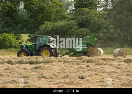 Grande Ouseburn, North Yorkshire, GB, Regno Unito - Balla rotonda & caduta caduta da un'imballatrice tirato da un green farm il trattore lavora in un campo, rendendo il foraggio insilato. Foto Stock