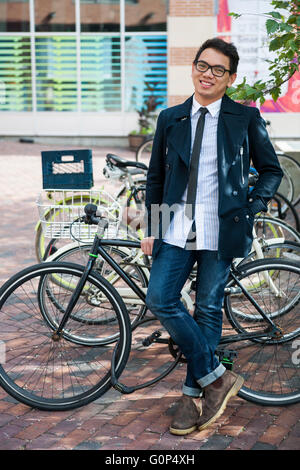 Giovani asiatici sorridente uomo d affari o studente in piedi nella parte anteriore della bicicletta rack parcheggio su strada di città Foto Stock