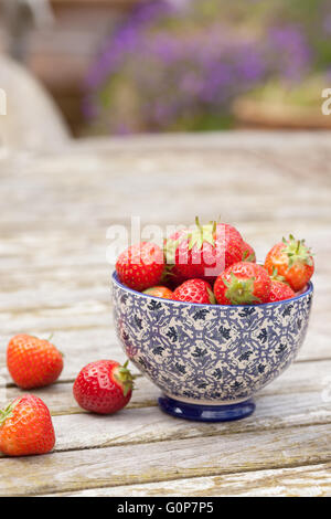 Fragole intere accanto a uno stile cinese ciotola piena di fragole su un di legno Tavolo da giardino Foto Stock