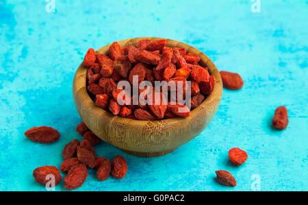 Bacche di Goji nella ciotola di legno dipinta su uno sfondo di legno Foto Stock