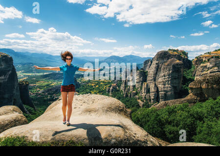 Giovane donna felice sorge torna alla roccia con le mani alzate. Traveler godendo il paesaggio, Meteora, Grecia Foto Stock