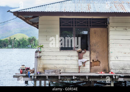 JAYAPURA, INDONESIA - circa Febbraio 2016: piccolo ragazzo di Papua cercando di salire in una casa attraverso una finestra Foto Stock