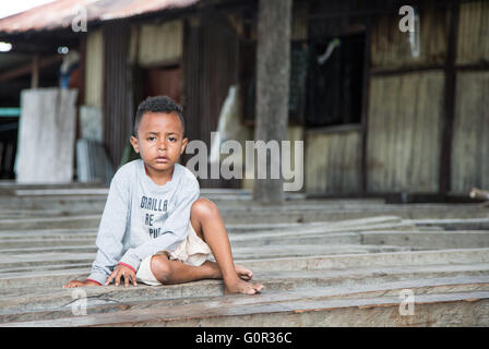 JAYAPURA, INDONESIA - circa Febbraio 2016: piccolo ragazzo di Papua, cercando di malessere e triste, seduta Foto Stock