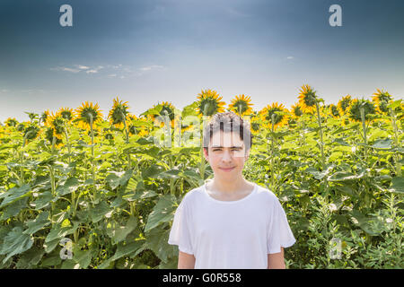 Naturali e uno stile di vita sano - Caucasian boy sorridere di fronte ad un campo di girasoli Foto Stock