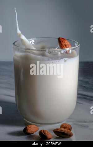 Spruzzi di mandorle in un bicchiere di latte di mandorla sulla tavola di marmo Foto Stock