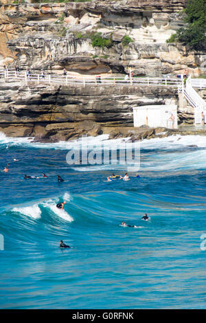 Surfers cattura le onde e walkers sulla passeggiata costiera a Bronte Beach, Sydney. Foto Stock