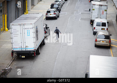 New york vista dalla linea alta guidatore di skateboard scoots lungo la strada di macchine parcheggiate furgoni Foto Stock