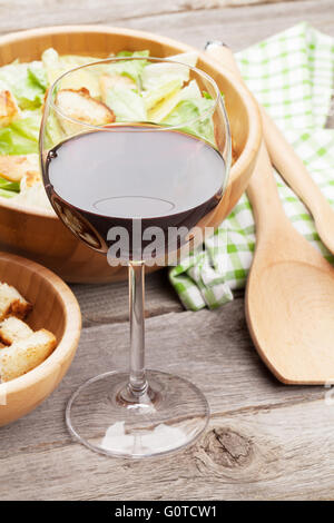 Il vino rosso di vetro e insalata caesar sul tavolo di legno Foto Stock