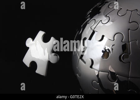 Floating pezzo del puzzle su chrome puzzle globe Foto Stock