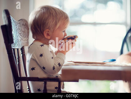 Ragazzo seduto nella sedia alta mangiare pancake Foto Stock