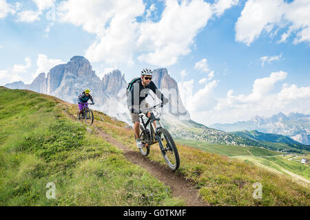 Un uomo e una donna in mountain bike racing lungo il sentiero nelle Dolomiti, Val Gardena, Italia Foto Stock