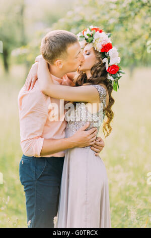 Sorridenti donna bionda in abito di lilla e corona baciare uomo bello indossare magliette di pesche Foto Stock