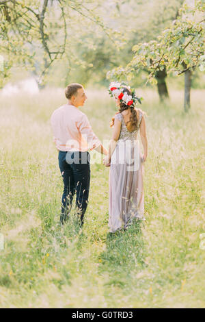 Matura in amore passeggiate all'aperto Holding Hands, attraente giovane uomo e donna che indossa corona sulla data, guardando ogni altro, vista posteriore Foto Stock