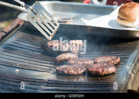 Gli hamburger e salsicce di essere cucinati su un barbecue Foto Stock