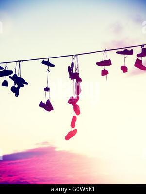 Vintage tonica sagome di scarpe appeso sul cavo al tramonto, ribellione adolescenziale concetto. Foto Stock